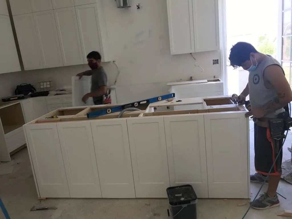 RM team installing white kitchen cabinetry, with a level across the unfinished island.